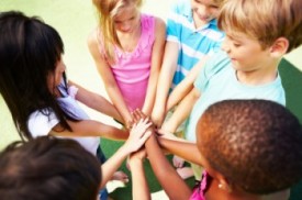 An image of children standing in a circle, placing their hands in a pile.