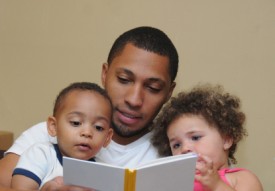 An image of an adult man reading to a little boy and a little girl