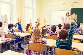 An image of a classroom of children raising their hands.