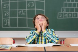 An image of a child in a classroom, sitting at a desk, with his head in his hands.