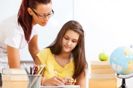 Image of a woman writing on a piece of paper that is laid out in front of a girl.