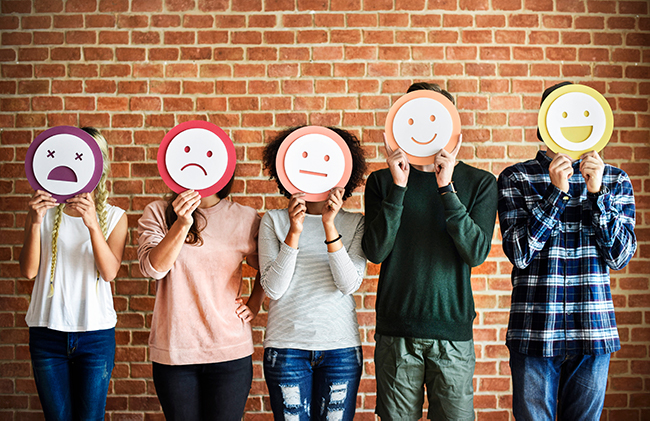 five teenagers holding paper faces over their faces, ranging from upset to very happy
