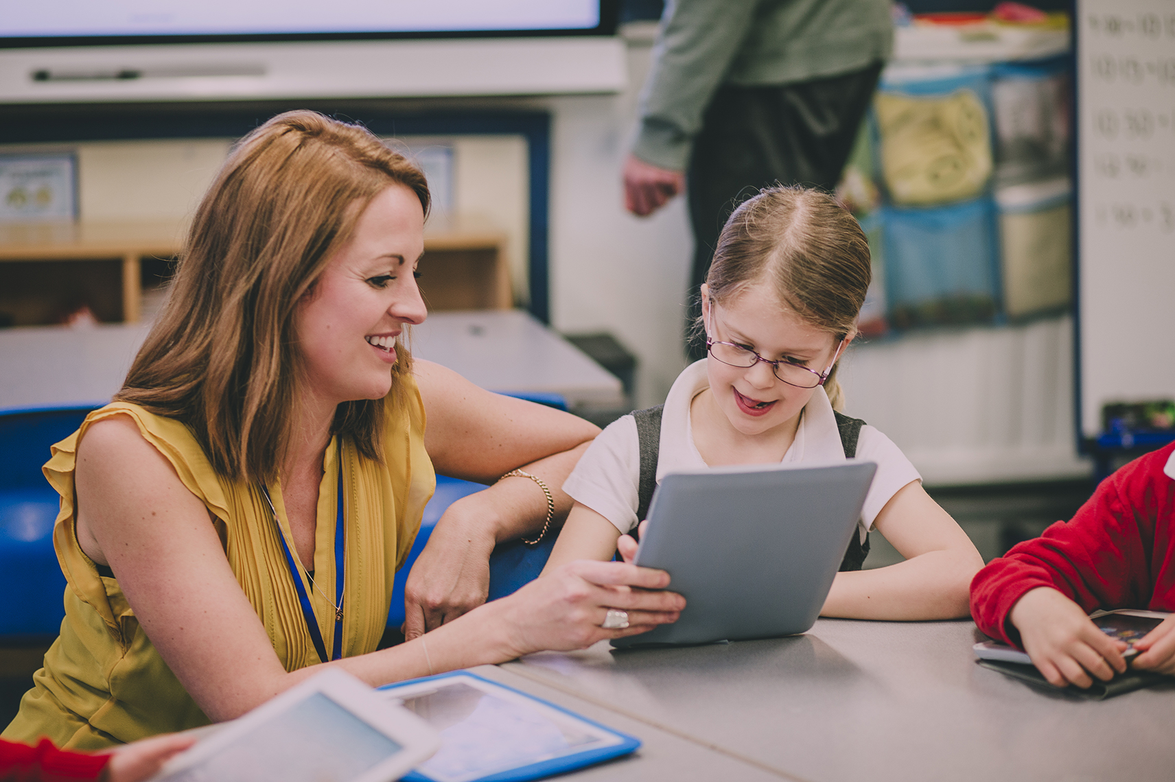 Teacher trust Fast ForWord; a teacher working with an elementary student on a tablet at a classroom table